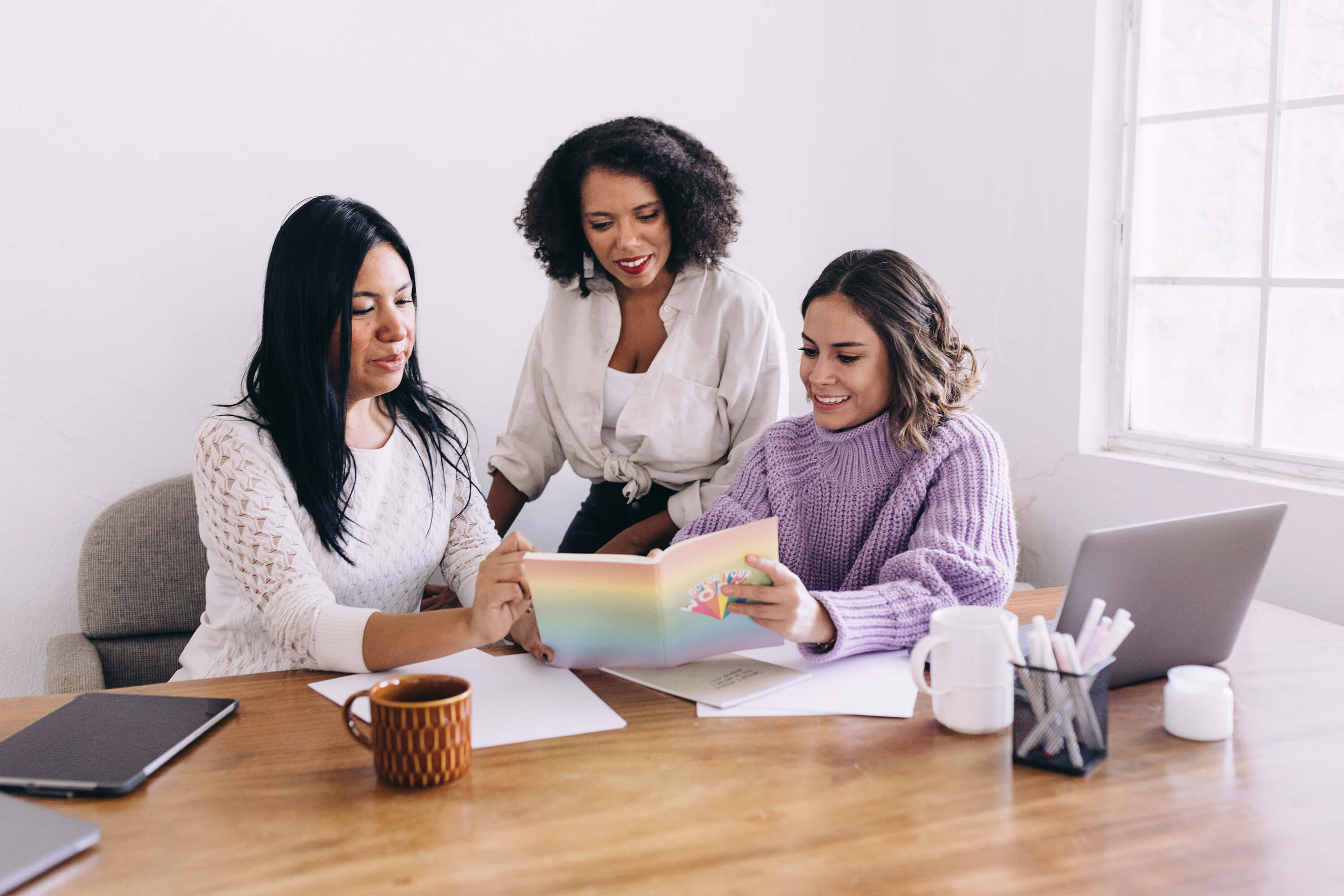 3 women working together at a table looking at a journal